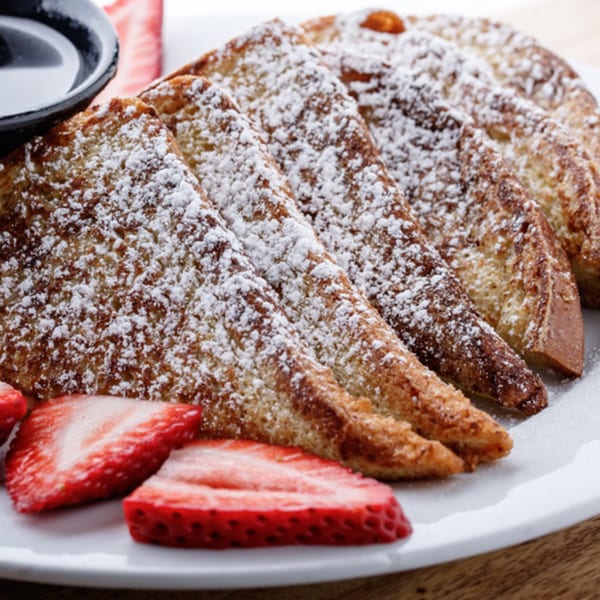 French toast triangles dusted with powdered sugar, served with sliced strawberries and syrup.